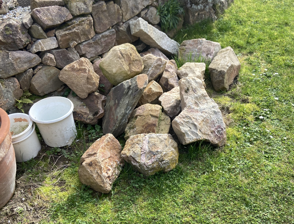 Zu sehen ist ein Bild von einigen Bruchsteinen vor einer Gartenmauer. Zu sehen ist ein Bild von einigen Bruchsteinen vor einer Gartenmauer.