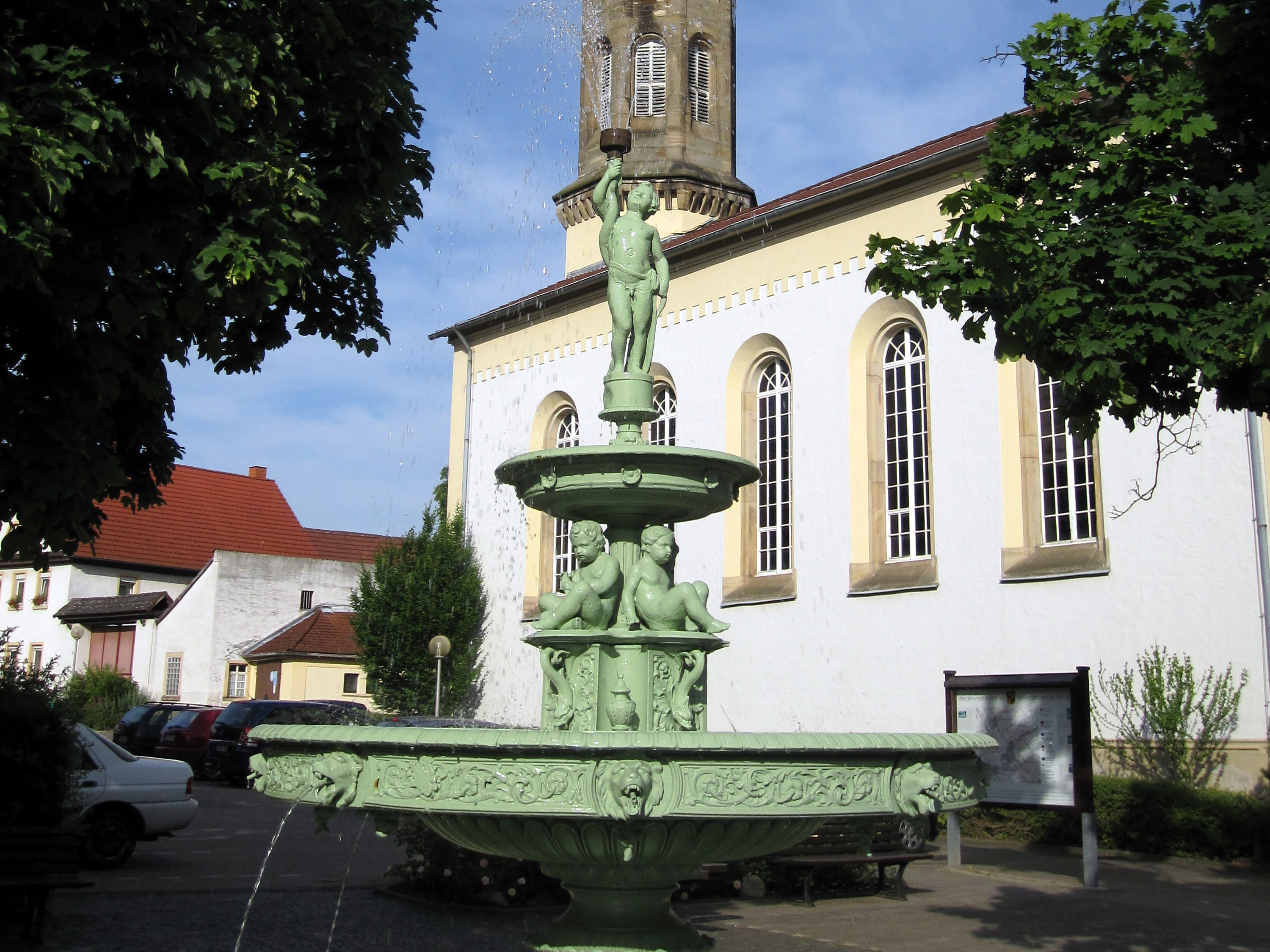 Zu sehen ist der Marktbrunnen in Schwabenheim. Im Hintergrund die evangelische Kirche.